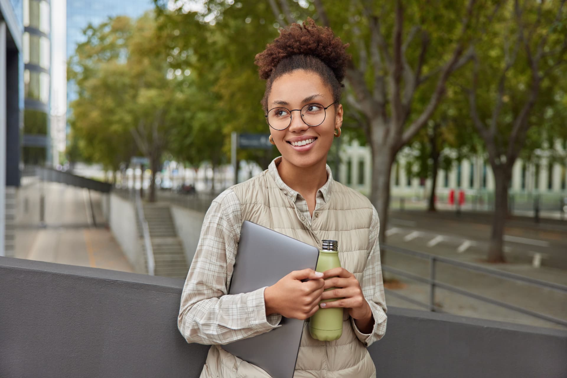 Jovem com laptop e garrafa térmica em ambiente urbano